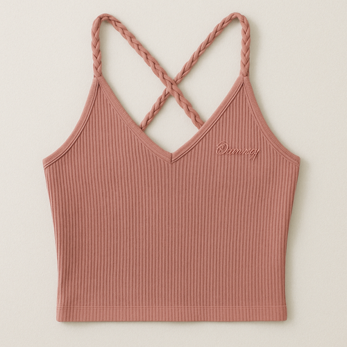 A fitted, feminine tank top inspired by the attached reference. The fabric is soft ribbed cotton in a dusty rose tone, designed to gently hug the body with a smooth, sculpted fit and cropped length just above the waist. The front features a modest draped V-neckline with braided straps for texture and detail. The back has crossed braided straps, but with a shallower scoop—not a deep V—providing more coverage while maintaining a graceful open-back look. The overall silhouette should appear sleek, minimal, and modern, with less fabric drape and no loose folds. Add delicate embroidery of the word “Beauty” in subtle tonal stitching near the right neckline to reflect the Beauty for Ashes theme.