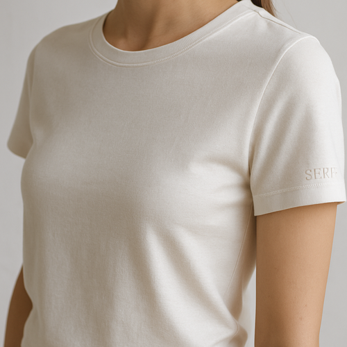A premium women’s basic crew neck t-shirt, slim-relaxed fit, high-quality cotton fabric, short sleeves, minimal and elegant design. On the left sleeve, near the cuff, a small embroidered SERF logo detail, subtle stitched embroidery with thread texture, luxury monogram style. Photographed in natural daylight, clean white background, ultra-detailed fabric texture, hyperrealistic cotton stitches, 3D depth of field close-up, fashion e-commerce product photography aesthetic.


